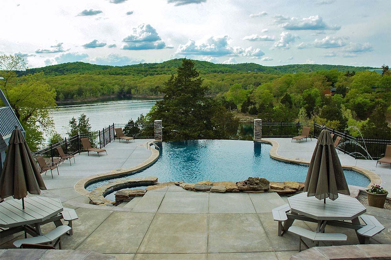 Large poolside sunbathing patio with tables, benches, umbrellas and chaise lounges at Alpine Lodge Resort, Branson, Missouri.
